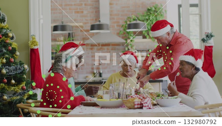 Group of five senior friends sharing holiday meal at wooden table in kitchen, with Santa hats 132980792