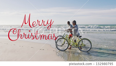 Walking couple pushing green beach cruisers on beach, with Merry Christmas text, copy space Walking couple pushing green beach cruisers on beach, with Merry Christmas text, copy space 132980795