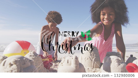 Building siblings in swimsuits constructing sandcastles at beach, with red bucket and beach ball 132980806