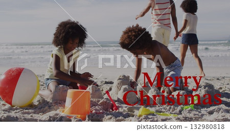 Two children building sandcastle at shoreline beach, using buckets, shovels and striped beach ball Two children building sandcastle at shoreline beach, using buckets, shovels and striped beach ball 132980818