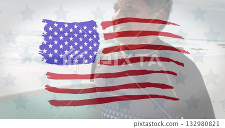 Holding surfboard senior surfer wearing wetsuit on sandy beach, with flag overlay, copy space 132980821