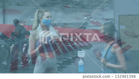 Standing workout partners wearing face masks and holding towel, band in gym with sanitizer station 132981398