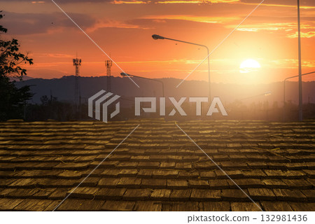 Wooden roof tiles glowing under warm sunlight during sunset with communication towers and hills in background. Natural texture, architectural detail, and peaceful countryside evening atmosphere. 132981436