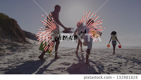 Walking family in swimwear along sandy shoreline at beach, with green tote, bodyboard and buckets 132981828