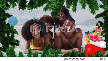 Lying swimwear-clad family smiling on sandy shore, with towels, pine branch, gift boxes, snowflakes 132981841