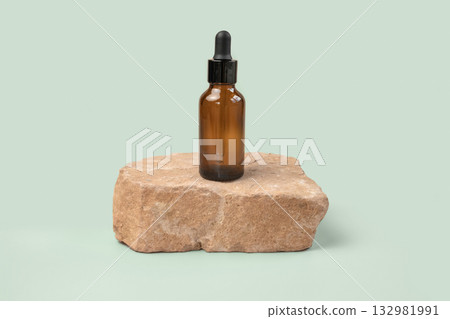 Dark amber glass bottle standing on stone. Natural skin care SPA beauty product design. Mineral organic oil cosmetics. Green background. MockUp. Oily pipette. Face and body treatment. Front view stand 132981991