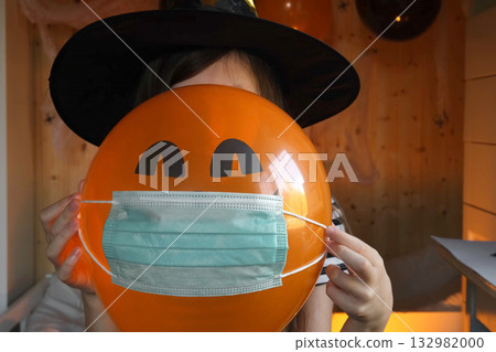 Halloween kids mask. Teen girl in witch costume and black hat. Child in protective medical mask waving hand during online call. Halloween. Protecting from COVID-19. Alternative safe celebration. Halloween kids mask. Teen girl in witch costume and black hat. Child in protective medical mask waving hand during online call. Halloween. Protecting from COVID-19. Alternative safe celebration. 132982000