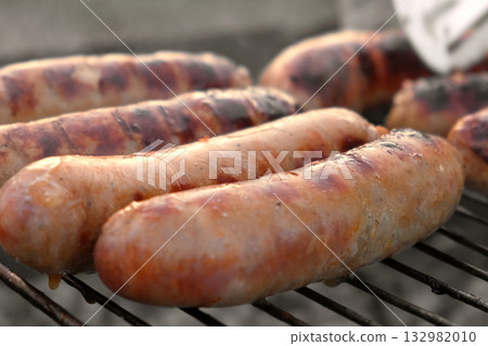 Grilled sausages. Cook man preparing grilling food bbq. Barbecue with smoke, flame outdoors. Tasty juicy german bratwurst. Charcoal kettle grill outside in backyard. Family summer vacation. Close-up 132982010