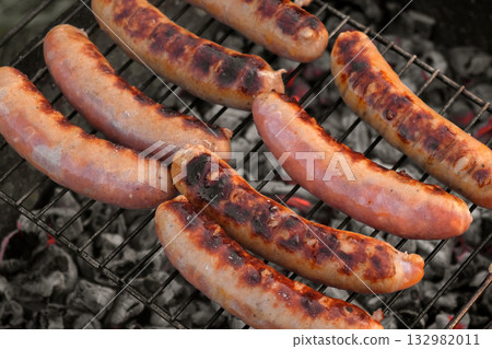Grilled sausages. Cook man preparing grilling food bbq. Barbecue with smoke, flame outdoors. Tasty juicy german bratwurst. Charcoal kettle grill outside in backyard. Family summer vacation. Close-up Grilled sausages. Cook man preparing grilling food bbq. Barbecue with smoke, flame outdoors. Tasty juicy german bratwurst. Charcoal kettle grill outside in backyard. Family summer vacation. Close-up 132982011
