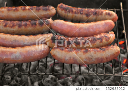 Grilled sausages. Cook man preparing grilling food bbq. Barbecue with smoke, flame outdoors. Tasty juicy german bratwurst. Charcoal kettle grill outside in backyard. Family summer vacation. Close-up 132982012