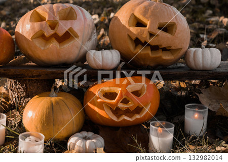 Halloween Pumpkin Head with Carved Scary Smiling Face on Wood Bench Outside. Jack-O-Lantern, Burning Candles, Dried Leaves Outdoors. Halloween Composition for Backyard Decor. Pumpkins. All Saints Day. Halloween Pumpkin Head with Carved Scary Smiling Face on Wood Bench Outside. Jack-O-Lantern, Burning Candles, Dried Leaves Outdoors. Halloween Composition for Backyard Decor. Pumpkins. All Saints Day. 132982014