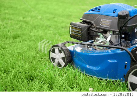 Lawn mower cutting grass. Small grass cuttings fly out of lawnmower. Grass clippings get spewed out of a mower pushed around by landscaper. CloseUp. Gardener working with mower machine. Mowing lawns Lawn mower cutting grass. Small grass cuttings fly out of lawnmower. Grass clippings get spewed out of a mower pushed around by landscaper. CloseUp. Gardener working with mower machine. Mowing lawns 132982015