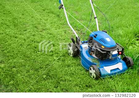 Lawn mower cutting grass. Small grass cuttings fly out of lawnmower. Grass clippings get spewed out of a mower pushed around by landscaper. CloseUp. Gardener working with mower machine. Mowing lawns Lawn mower cutting grass. Small grass cuttings fly out of lawnmower. Grass clippings get spewed out of a mower pushed around by landscaper. CloseUp. Gardener working with mower machine. Mowing lawns 132982120