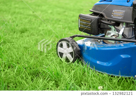 Lawn mower cutting grass. Small grass cuttings fly out of lawnmower. Grass clippings get spewed out of a mower pushed around by landscaper. CloseUp. Gardener working with mower machine. Mowing lawns 132982121