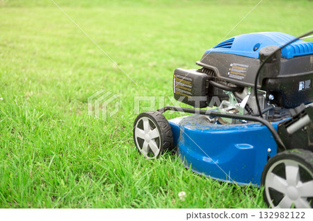 Lawn mower cutting grass. Small grass cuttings fly out of lawnmower. Grass clippings get spewed out of a mower pushed around by landscaper. CloseUp. Gardener working with mower machine. Mowing lawns Lawn mower cutting grass. Small grass cuttings fly out of lawnmower. Grass clippings get spewed out of a mower pushed around by landscaper. CloseUp. Gardener working with mower machine. Mowing lawns 132982122