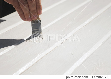Man painting wooden table outdoors. Renovation of garden furniture. Close up hand with paintbrush. Home improvement. Handyman varnishing wooden planks outside. Painting wooden surface with white dye Man painting wooden table outdoors. Renovation of garden furniture. Close up hand with paintbrush. Home improvement. Handyman varnishing wooden planks outside. Painting wooden surface with white dye 132982179