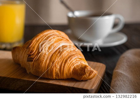 Coffee cup with croissant on a rustic dark wooden table. Food series. Two tasty fresh croissants, jam, orange juice. Continental breakfast served with freshly baked pastry. Close up view, Good morning Coffee cup with croissant on a rustic dark wooden table. Food series. Two tasty fresh croissants, jam, orange juice. Continental breakfast served with freshly baked pastry. Close up view, Good morning 132982216