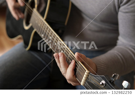 Playing the guitar. Strumming acoustic guitar. Musician plays music. Man fingers holding mediator. Man hand playing guitar neck in dark room. Unrecognizable person rehearsing, fretboard close-up Playing the guitar. Strumming acoustic guitar. Musician plays music. Man fingers holding mediator. Man hand playing guitar neck in dark room. Unrecognizable person rehearsing, fretboard close-up 132982250