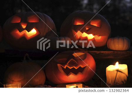 Halloween Pumpkin Head with Carved Scary Smiling Face at Night Outside. Jack-O-Lantern, Burning Candles Outdoor. Halloween Dark Composition Backyard Decor. Pumpkins Black Background. All Saints Day 4K 132982364