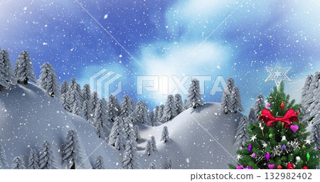 Standing Christmas tree topped with star under falling snow among evergreens in hills, copy space 132982402