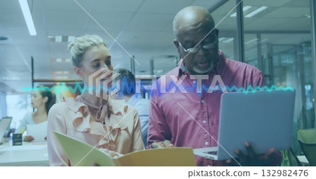 Mentor in red shirt and coworker in pink blouse examining laptop at office, with yellow folder 132982476