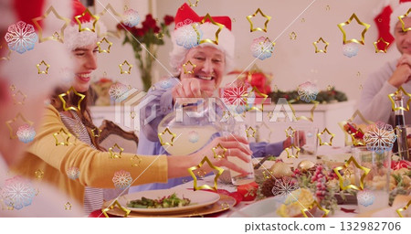 Smiling senior in Santa hat pouring drink into granddaughter tumbler at dining table, with pitcher 132982706