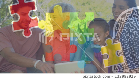 Watching extended family viewing tablet on garden bench, with floating colorful puzzle graphics 132982929