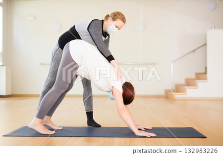 Pregnant woman practices yoga with an instructor wearing an antiviral mask during quarantine. Downward Dog Pose or Adho Mukha Svanasana Pregnant woman practices yoga with an instructor wearing an antiviral mask during quarantine. Downward Dog Pose or Adho Mukha Svanasana 132983226