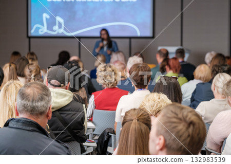 Speaker presents to engaged audience at conference with large screen presentation in a modern hall 132983539