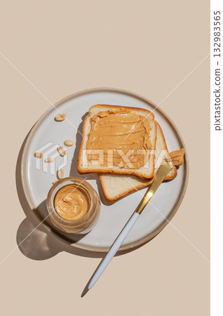 Peanut butter toast with jar of spread, nuts and knife on a plate on a light background. Peanut butter toast with jar of spread, nuts and knife on a plate on a light background. 132983565