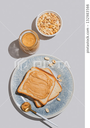 Peanut butter toast on a plate on a blue background with jar of spread, nuts, spoon Peanut butter toast on a plate on a blue background with jar of spread, nuts, spoon 132983566