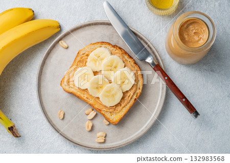 Peanut butter toast on a plate on a light background with banana, nuts and knife 132983568