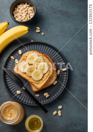 Peanut butter toast and banana on a black plate on a dark background with nuts 132983578