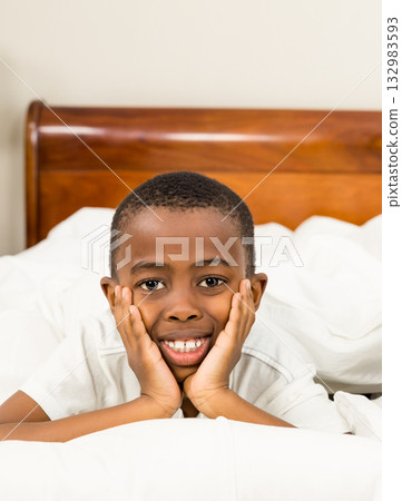 African American boy lying on bed with white sheets and pillows in bedroom, resting and smiling 132983593