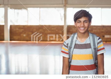 Teenage boy standing on right side in school gym carrying gray backpack, copy space Teenage boy standing on right side in school gym carrying gray backpack, copy space 132983605