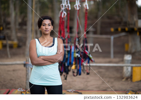 Woman in sportswear standing with arms crossed in front of safety gear at aerial adventure park 132983624