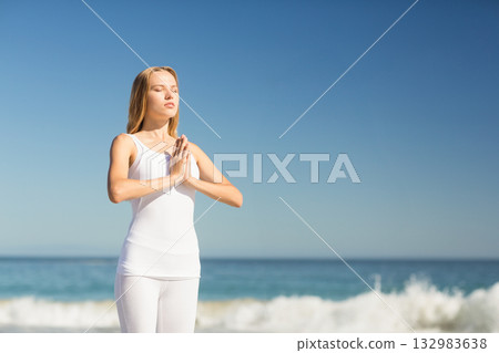 Woman wearing white workout clothing practicing meditation on beach facing waves copy space 132983638