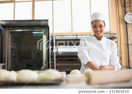 African American woman kneading dough with rolling pin on steel table in bakery, copy space African American woman kneading dough with rolling pin on steel table in bakery, copy space 132983650