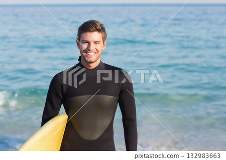 Male surfer wearing black wetsuit wading waist-deep at sandy shore holding yellow surfboard smiling Male surfer wearing black wetsuit wading waist-deep at sandy shore holding yellow surfboard smiling 132983663