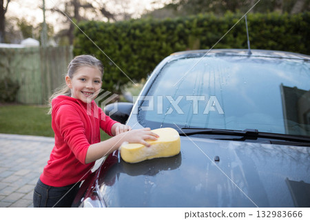 Child in red hoodie scrubbing car hood on driveway with large sponge, suds, copy space 132983666
