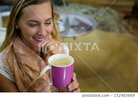 Woman sitting at coffee table wearing peach polka dot scarf holding large pink mug at home 132983669