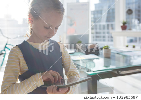 Female child tapping on tablet in office beside bicycle frame and conference table with succulents Female child tapping on tablet in office beside bicycle frame and conference table with succulents 132983687