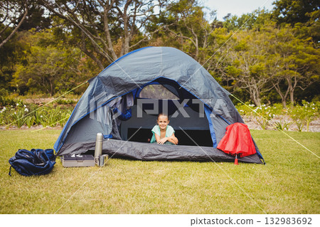 Girl leaning into gray dome tent in forest clearing with sleeping bag, thermos and red jacket Girl leaning into gray dome tent in forest clearing with sleeping bag, thermos and red jacket 132983692