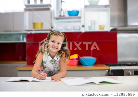 Girl writing in open notebook on kitchen countertop using pink pencil near bowls and refrigerator Girl writing in open notebook on kitchen countertop using pink pencil near bowls and refrigerator 132983699