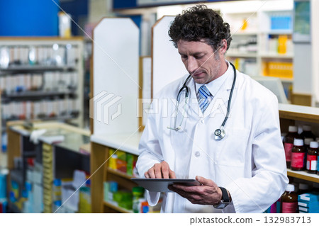 Senior male doctor wearing stethoscope using tablet at pharmacy with medicine bottles copy space 132983713