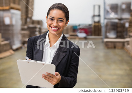 Smiling African American woman in blazer holding clipboard and pen, inspecting stock in warehouse Smiling African American woman in blazer holding clipboard and pen, inspecting stock in warehouse 132983719
