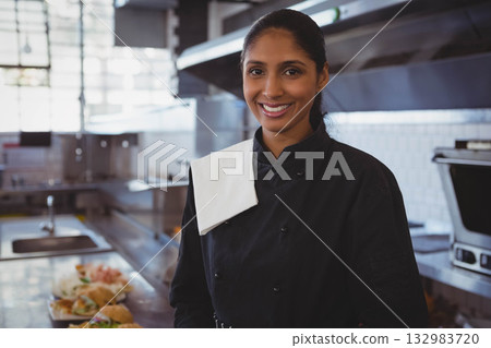 Indian female chef wearing black jacket smiling in kitchen by prep counter with plated sandwiches Indian female chef wearing black jacket smiling in kitchen by prep counter with plated sandwiches 132983720