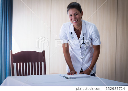 Female nurse leaning on table with notebook in clinic wearing uniform and stethoscope, copy space Female nurse leaning on table with notebook in clinic wearing uniform and stethoscope, copy space 132983724