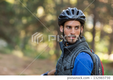 Man pausing on wooded trail wearing bicycle helmet and backpack, noticing dappled light, copy space Man pausing on wooded trail wearing bicycle helmet and backpack, noticing dappled light, copy space 132983730