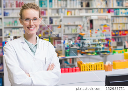 Female pharmacist wearing coat using dispensing trays and monitor at pharmacy counter, copy space 132983751